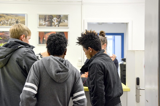 Drei junge Männer stehen am Schalter und werden von einer Frau beraten