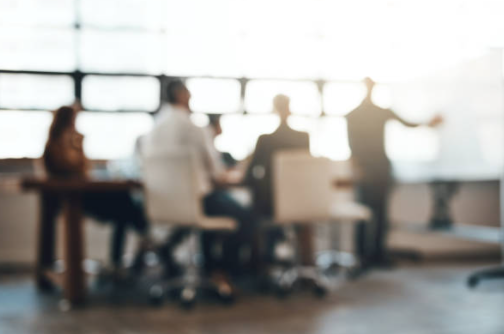 Personen sitzen um einen Tisch und verfolgen Präsentation einer Person mit Flipchart